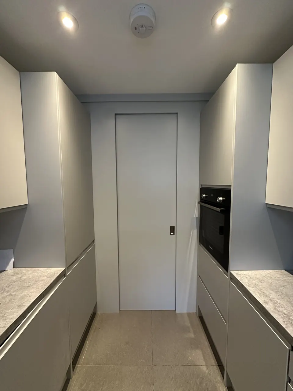 Tall grey kitchen units and flush door at the end of a galley kitchen
